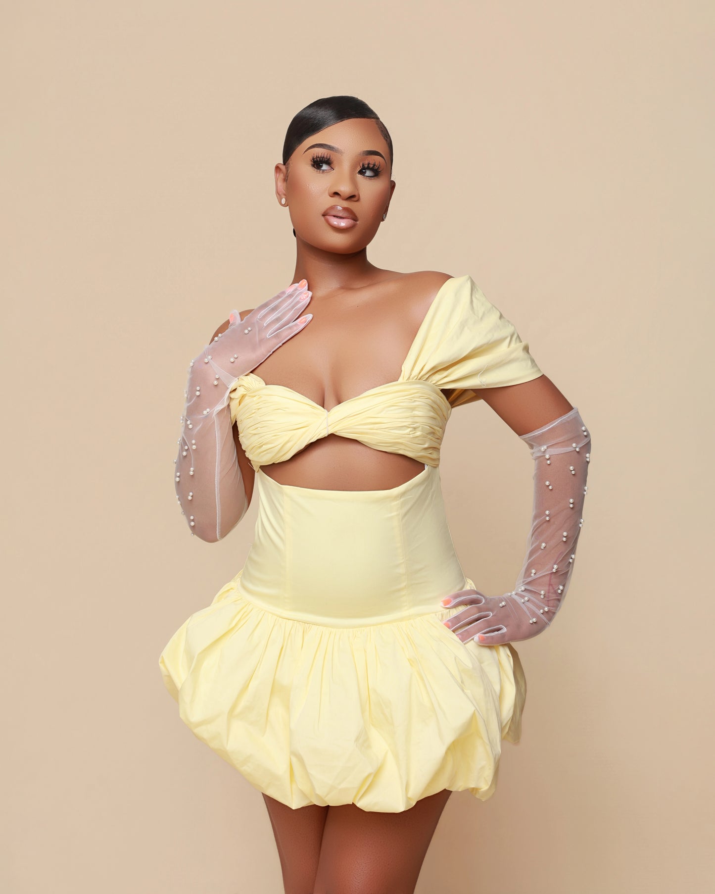 Woman wearing a yellow dress with sheer gloves against a beige background