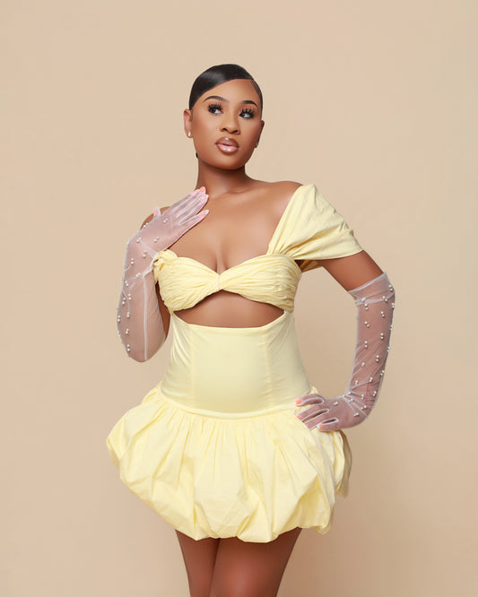 Woman wearing a yellow dress with sheer gloves against a beige background