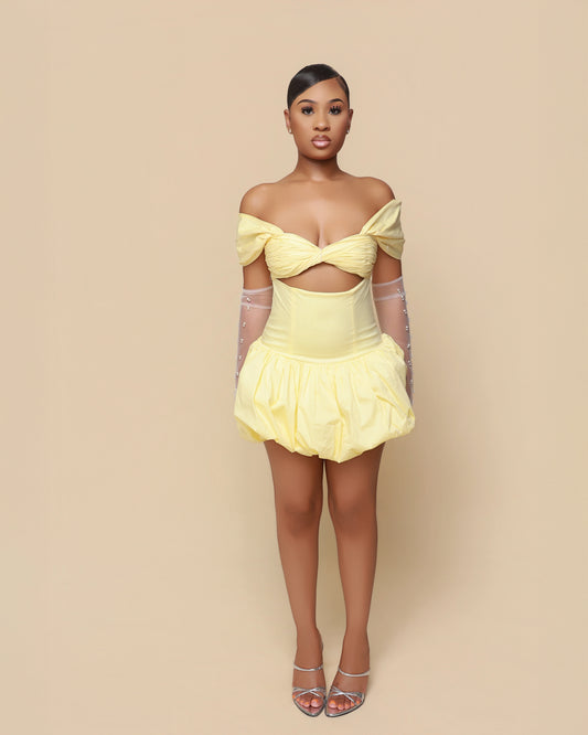 Woman wearing a yellow off-shoulder dress with sheer sleeves against a beige background